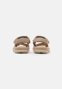 Tan sandals with straps, featuring a textured finish and adjustable buckle closures. Thick cushioned soles for comfort. Back view shown.