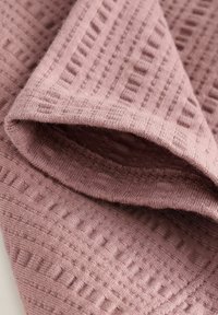 Strukturiertes pinkes Stoffmaterial mit einem gestrickten Muster, das abwechselnd erhabene und flache Abschnitte aufweist. Weich, mit sauber gesäumtem Rand.