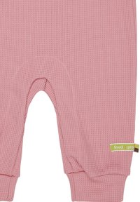 Roze waffle-gebreide romper met een ronde opening voor eenvoudig verschonen, ribgebreide manchetten en een groene label die de zijkant accentueert.