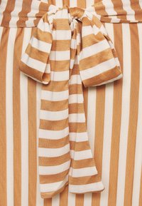 Tkanina w paski z naprzemiennymi złotymi i białymi liniami, z kokardą zawiązaną na środku. Materiał wydaje się miękki i teksturowany.