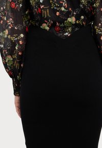 Μαύρη ριχτή φούστα συνδυασμένη με διαφανή μπλούζα με λουλουδάτο σχέδιο, που διαθέτει φουσκωτά μανίκια και λαιμόκοψη σε V.