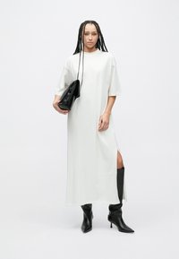 Hvit kjole til kneet med korte ermer og sidespalter. Teksturert, glatt stoff. Sorte høyhælte støvler og en svart clutch-veske.