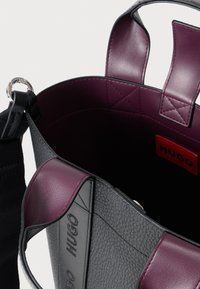Geantă tote din piele neagră cu căptușeală interioară de culoare burgundy închis, având panouri netede și texturate, și o etichetă cu logo în interior.