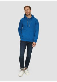 Blauwe hoodie van katoen, met een voorzak, een capuchon met trekkoord en een witte logo-opdruk. Gecombineerd met donkere jeans en witte sneakers.