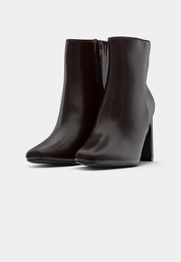 Pair of dark brown leather ankle boots with high block heels and side zippers on a white background.