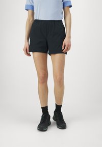 Svart treningsshorts med elastisk midje. Modellen har dem på seg med en lyseblå skjorte og svarte sko, som viser en minimalistisk design.