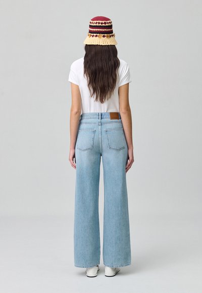 Jean large bleu clair à taille haute avec poches arrière, associé à un t-shirt blanc et un chapeau seau tissé multicolore.