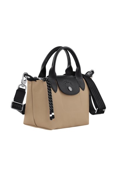 Beige tote bag with black leather accents and handles. Features a removable black strap and polka-dot ties. Compact design with textured materials.