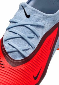 Scarpa da calcio Nike blu e rossa con tomaia testurizzata, lacci prominenti e suola liscia con scanalature accentuate e dettagli di branding.