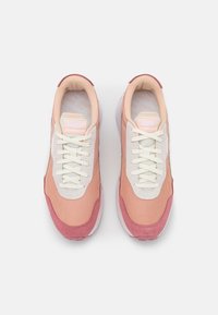 Ett par rosa och beige Puma-sneakers med vita snören och vadderade kragar sett ovanifrån på en vit bakgrund.