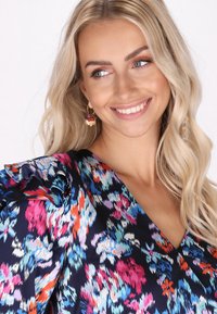 Šaty s květinovým potiskem v námořnické modři, zdobené barevnými vzory růžové, modré a oranžové. Rukávy s volánky a hladká textura. Dekorativní náušnice.