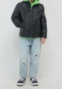 Czarna skórzana kurtka z zamykanymi na zamek kieszeniami, nałożona na zieloną bluzę z kapturem. Jasnoniebieskie dżinsy z przetarciami, noszone z czarnymi trampkami.