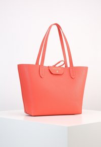 Koralowa skórzana torba na ramię z dwoma uchwytami, teksturowana powierzchnia oraz zapięcie na klapkę z logo i złotymi elementami. Prostokątny kształt.