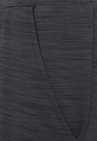 Primer plano de una tela texturada de color gris oscuro con costuras en capas superpuestas que forman un sutil patrón geométrico.