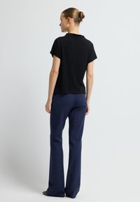 Top negro de manga corta con puños enrollados, combinado con pantalones rectos azul marino. Tela suave, diseño minimalista y sin patrones visibles.