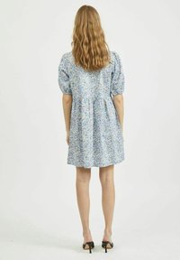 Robe à motif floral en bleu clair avec manches bouffantes et taille froncée. Portée avec des sandales à talons noires.