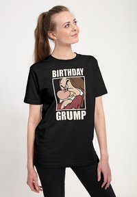 Maglietta nera con il volto di un personaggio dei cartoni animati caratterizzato da tratti esagerati. La scritta "BIRTHDAY GRUMP" è in lettere bianche e in grassetto.