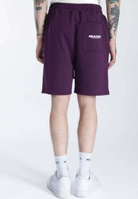 Shorts de sport violets foncés avec une taille élastique, une poche arrière et un logo. Fabriqués en tissu doux, lavables en machine, au design arrivant aux genoux.