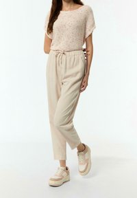 Top a maglia rosa chiaro con maniche corte, abbinato a pantaloni beige con laccetto e sneakers color crema con accenti rosa.