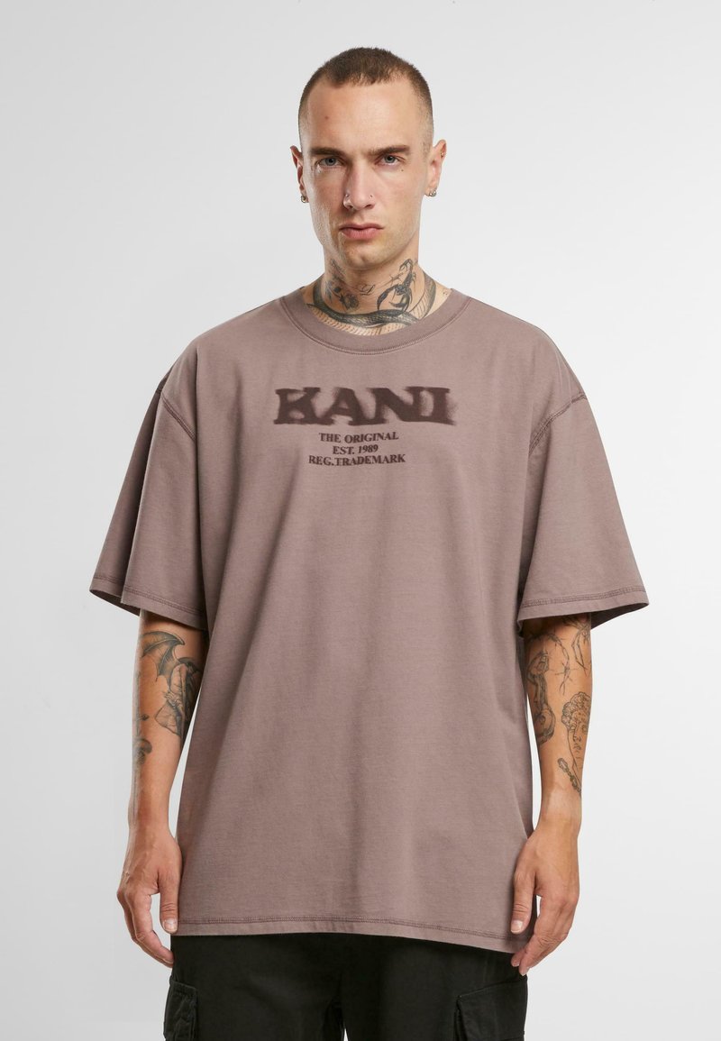 Brown oversized t-shirt made of cotton, featuring a subtle printed logo on the chest. Short sleeves and a relaxed fit with a round neckline.