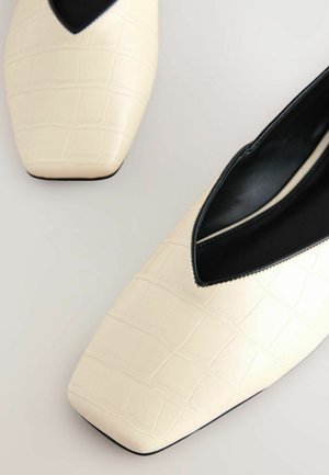 Ballet flats in pelle ivories decorate a stampa di coccodrillo con punta affilata e dettagli in pelle nera lungo l'apertura e l'interno. Texture liscia, design minimalista.