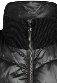 Schwarze gepolsterte Jacke mit hohem Strickkragen, ausgestattet mit einem Reißverschluss und glänzender Textur. Entwickelt für Wärme und Komfort.