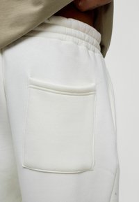 Witte katoenen sweatpants met een elastische tailleband en een decoratieve patch pocket aan de zijkant. Zachte textuur met zichtbare stiksel details.