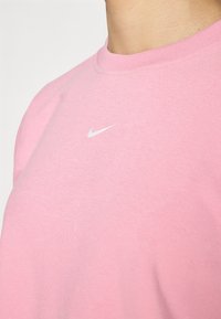 T-shirt en coton rose avec un col rond classique et des manches courtes. Présente un petit logo Nike blanc sur la poitrine. Texture douce et lisse.
