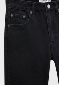 Détail d'un jean en denim noir montrant la poche avant, la petite poche, la passants de ceinture et un bouton en argent avec le nom de la marque Pull&Bear.