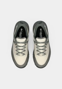 Chaussures de randonnée beiges et grises avec une tige texturée, un embout rond, des bords renforcés et des lacets gris à pois. Comporte un logo sur la semelle intérieure.