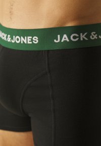 Zwarte boxershorts van een katoenmix met een groene elastische tailleband waarop de tekst "JACK & JONES" in het wit staat. Ze hebben een gladde textuur en een aansluitend ontwerp.