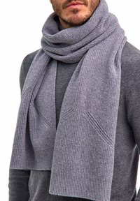 Uomo che indossa una sciarpa grigia spessa e a coste avvolta attorno al collo sopra un maglione grigio, tagliata sotto il naso.