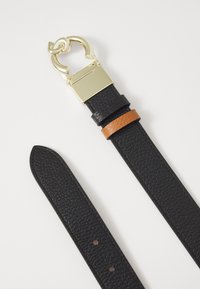 Cintura in pelle nera testurizzata con finiture dorate e una fascia accentuata in marrone a contrasto. Presenta una grande fibbia circolare e fori per la regolazione della misura.