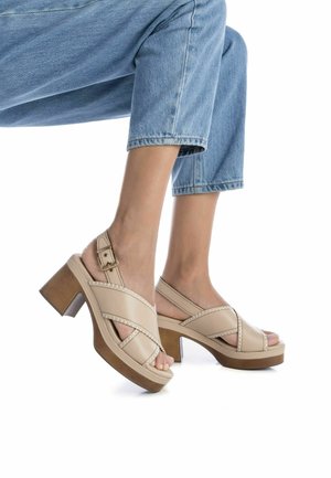 Sandalias de tacón beige con tiras cruzadas, hebilla ajustable en el tobillo, plataforma de textura madera y diseño de punta abierta.