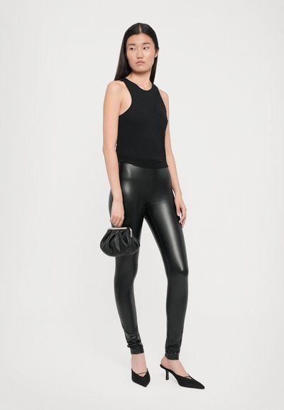 Musthave mustra, sobadused leggings ja terava ninaga mustad kontsad. Mudel hoiab käes väikest musta kotti, seistes neutraalse tausta ees.