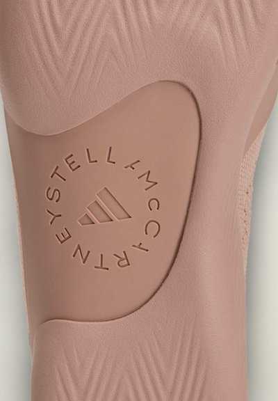 Suela de zapato rosa con superficie texturizada y un logotipo circular que dice "STELL McCARTNEY", con un diseño estilizado de tres franjas.