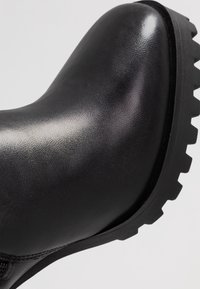 Mustat nahkaiset nilkkakengät, joissa on sileä pinta, pyöreä kärki ja kestävä, teksturoitu kumipohja. Varustettu kevyellä korolla.