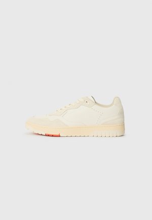 Cremfarbener Sneaker mit einem Obermaterial aus glattem Leder und Wildleder. Verfügt über eine strukturierte Sohle, subtile Perforationen und einen orangen Akzent auf der Sohle.