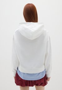 Witte hoodie met een zachte textuur, met een relaxte fit en een ribbelrand, gedragen over een blauw gestreept shirt en een kastanjebruine rok.