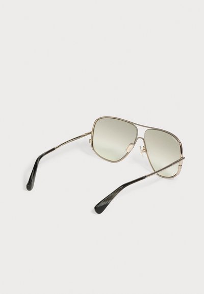 Une paire de lunettes de soleil style aviateur avec des fines montures métalliques dorées et des verres légèrement teintés sur fond blanc.