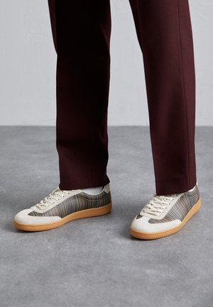 Beige vászon felsőrésszel készült sportcipő, amelyet színes vízszintes csíkok díszítenek, és texturált barna gumitalppal rendelkezik. Bordó nadrággal párosítva.