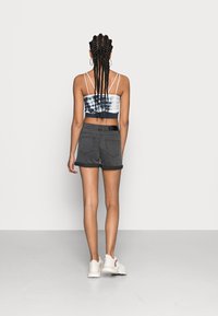 Svarta jeansshorts med uppvikta fållar, matchade med en tie-dye crop top. Modellen vänder ryggen; bär vita sneakers och har flätat hår.