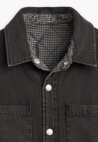 Zwarte denimshirt met een gewatteerde grijze geruite voering, drukknoopsluiting en een borstzak. Bevat een klassiek kraagontwerp.