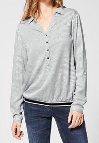 Blouse à manches longues en tissu léger à pois noirs et blancs, dotée d'un col, d'une patte de boutonnage et d'un ourlet rayé.