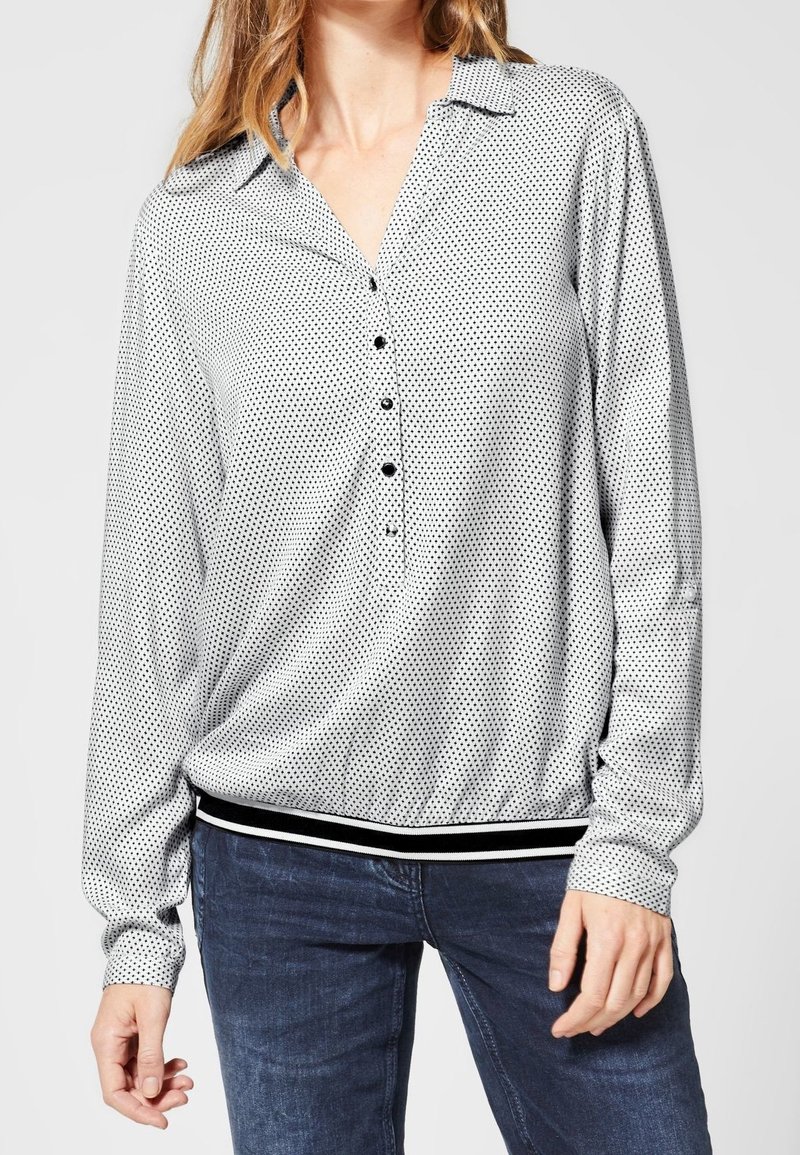 Blouse à manches longues en tissu léger à pois noirs et blancs, dotée d'un col, d'une patte de boutonnage et d'un ourlet rayé.