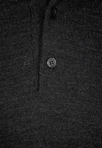 Dunkelgraues gestricktes Poloshirt mit einer Dreiknopf-Leiste, feiner Textur und einem kleinen Logo auf einem Knopf.