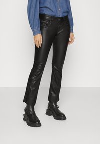 Czarne spodnie z sztucznej skóry o slim fit, z frontowymi kieszeniami i detalami na szwach, zestawione z czarnymi botkami za kostkę i dżinsową bluzką.