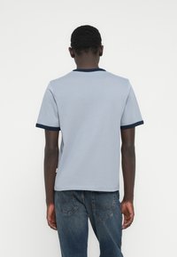 Ανοιχτό μπλε βαμβακερό t-shirt με κοντά μανίκια, στρογγυλή λαιμόκοψη σε ναυτικό μπλε και μονή υφή. Συνδυασμένο με μπλε τζιν παντελόνι.