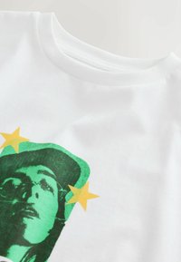 White cotton t-shirt featuring a green graphic of a face with green and yellow star accents, showcasing a round neckline and smooth texture.