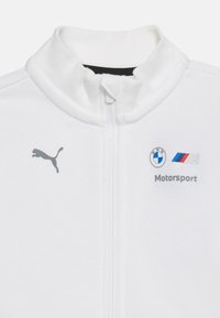 Λευκό μπουφάν με φερμουάρ και γιακά, με το λογότυπο της Puma στο αριστερό μέρος και τα λογότυπα της BMW Motorsport στη δεξιά πλευρά του στήθους.